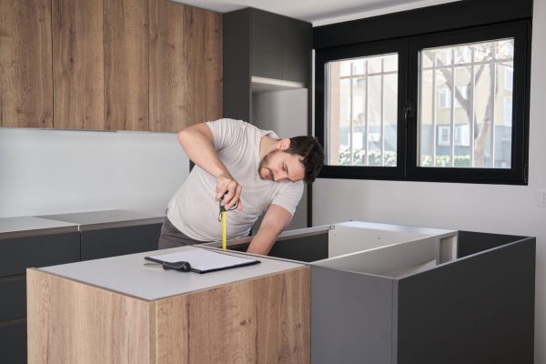 Young hispanic man using measuring tape before placing countertops on modern kitchen.